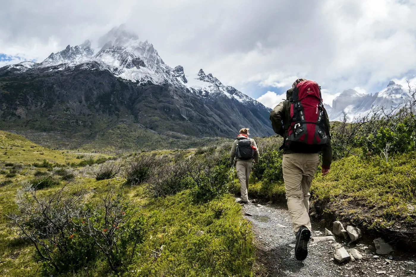 Two backpackers on a trail toward snowy peaks